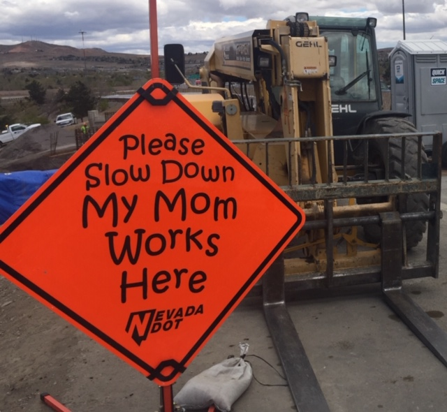 Orange road construction sign reading "My Mom Works Here" in childlike handwriting